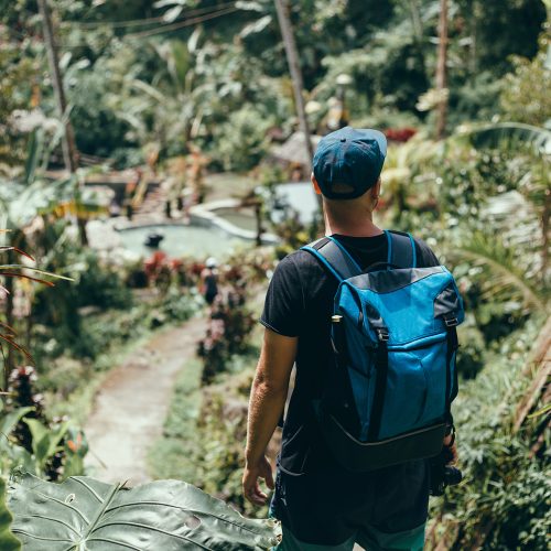 young guy with a beard and a backpack posing in the jungle in a cap